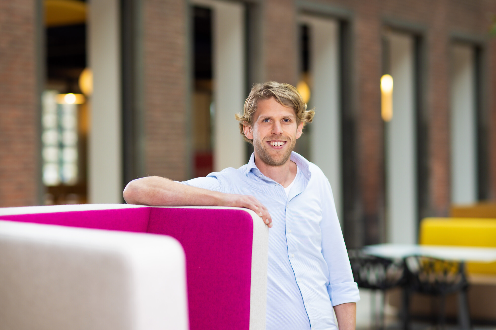 Man in lichtblauwe blouse leunend op magenta stoel