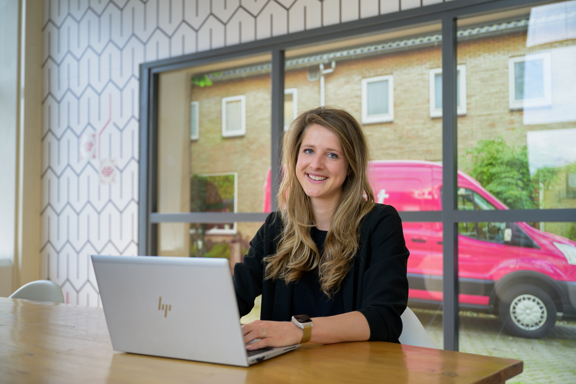 Vrouw glimlachend in camera achter laptop met roze Essent bus 