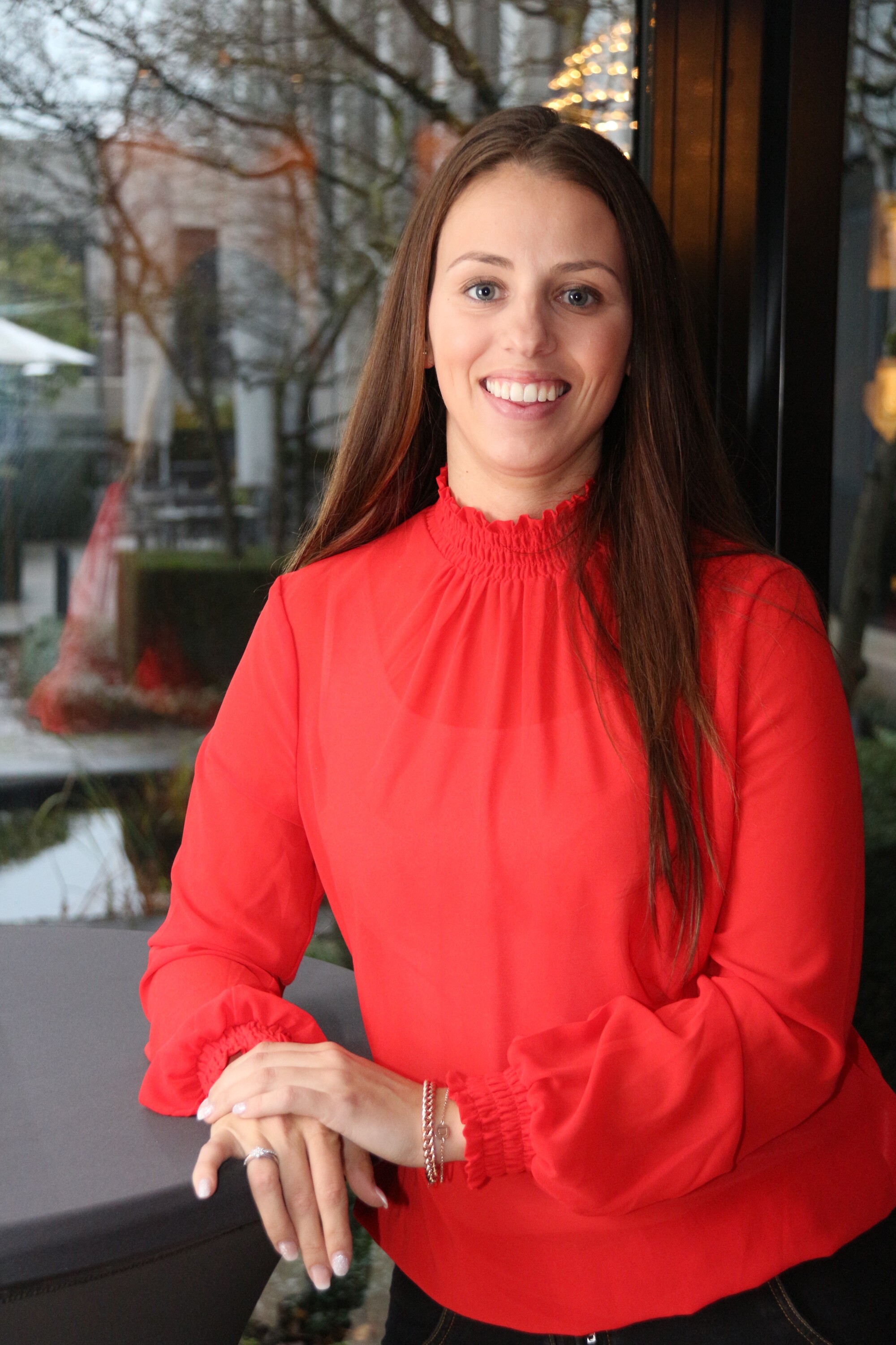 Vrouw met bruin lang haar en rode blouse lacht naar camera