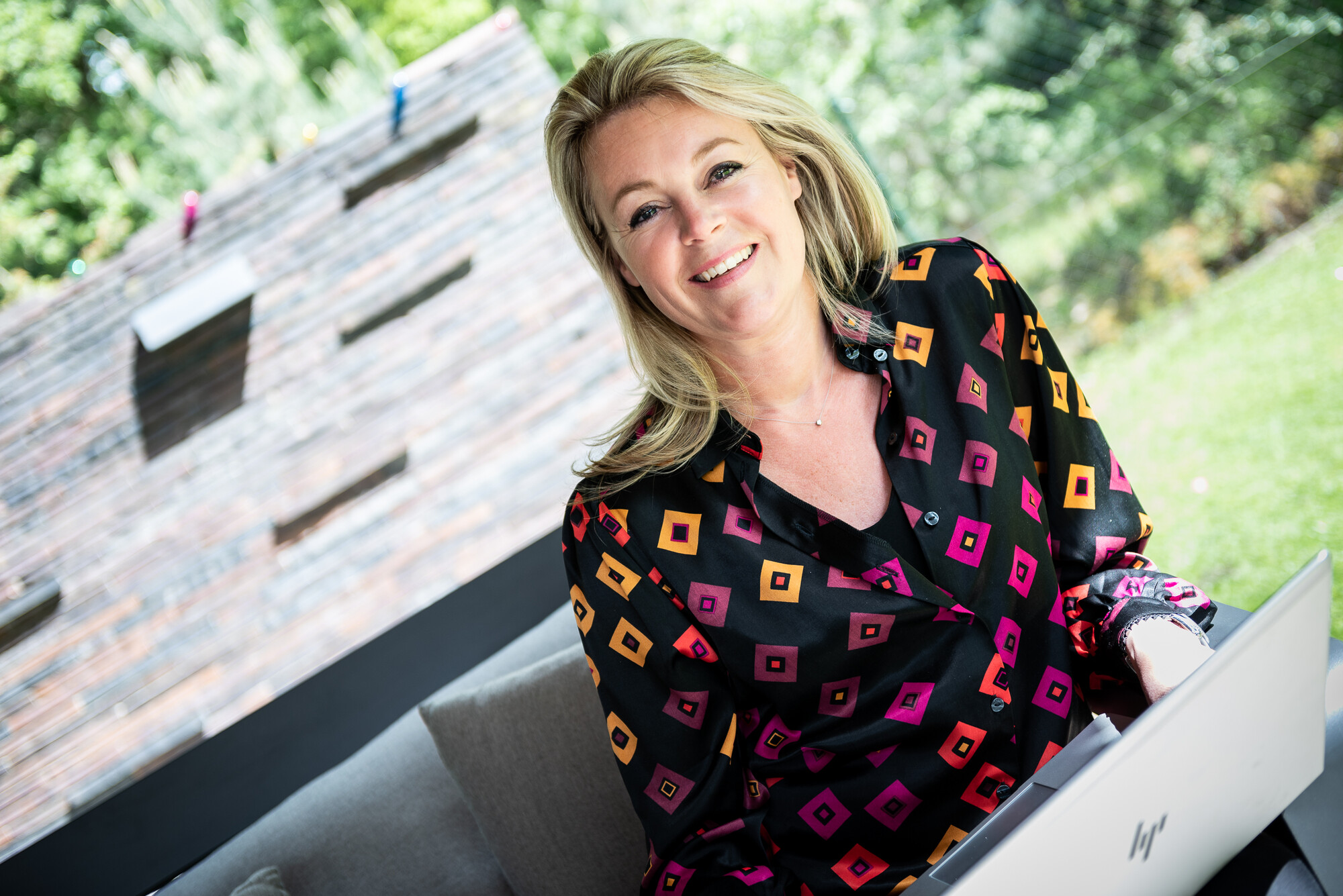 Vrouw met zwarte, roze, oranje blouse zittend achter laptop