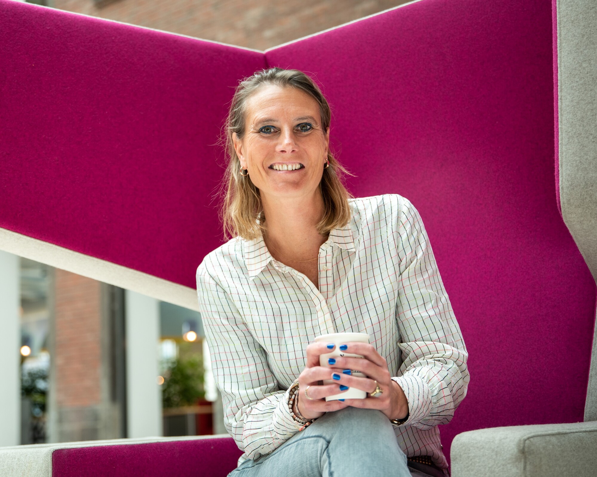 Vrouw met kop koffie in haar handen zittend op een magenta stoel