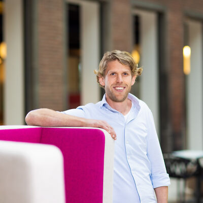 Man in lichtblauwe blouse leunend op magenta stoel