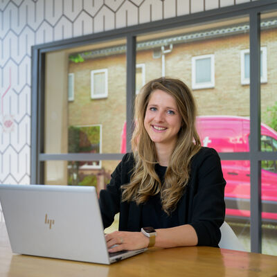 Vrouw glimlachend in camera achter laptop met roze Essent bus 