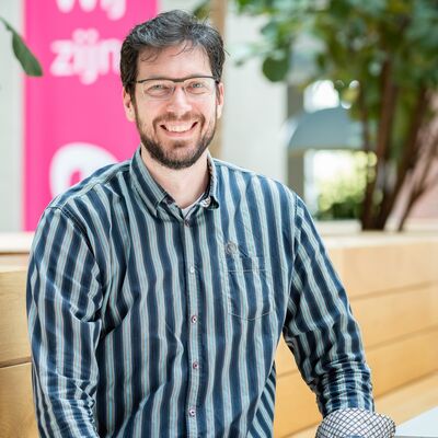 Man met groen gestreepte blouse en bril lacht naar de camera