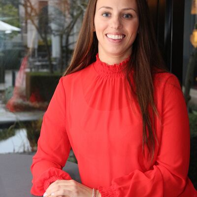 Vrouw met bruin lang haar en rode blouse lacht naar camera