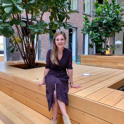 Dame in paarse jurk zittend op een houten bank met boom erachter