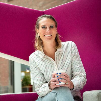 Vrouw met kop koffie in haar handen zittend op een magenta stoel